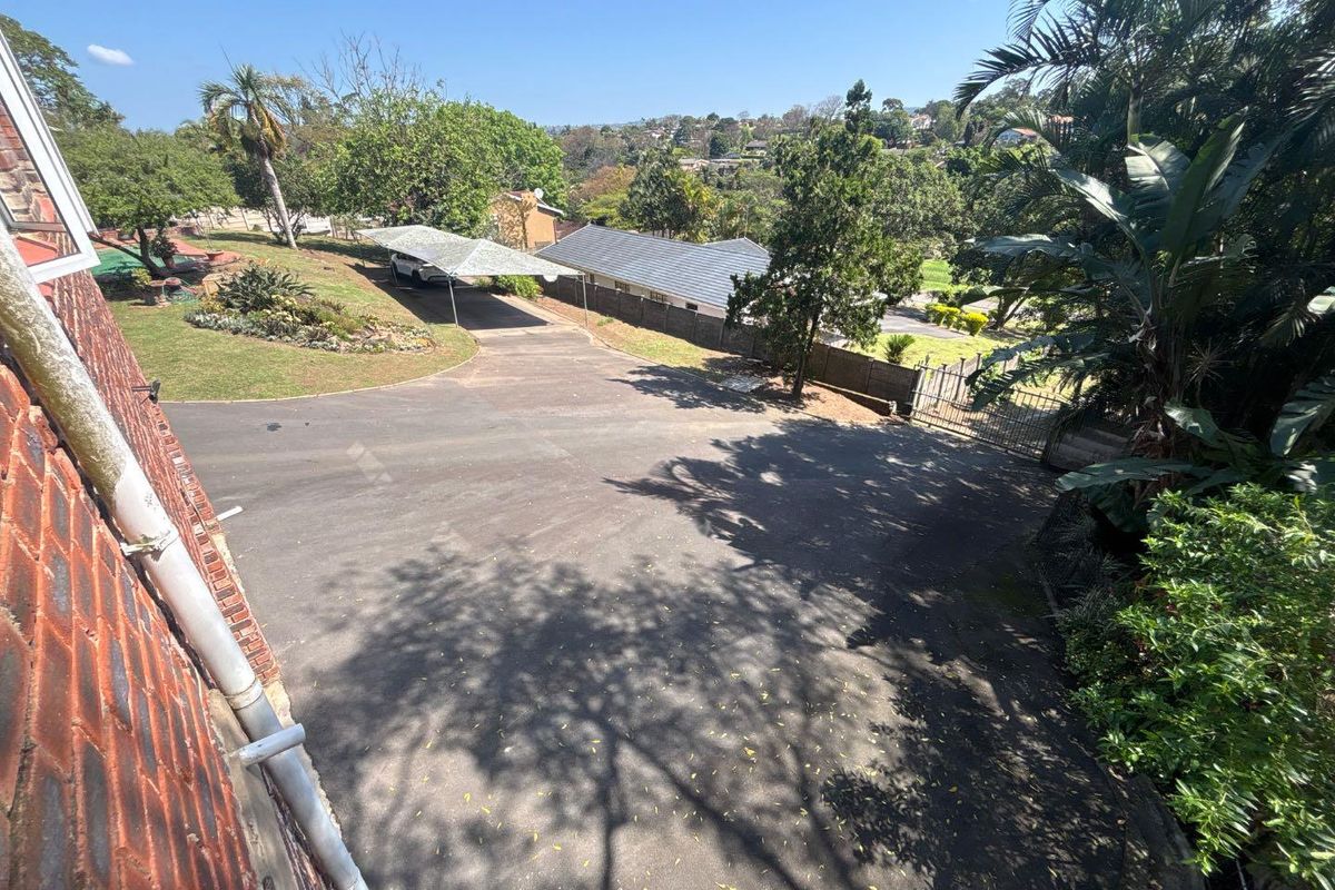 Aerial view of the property driveway, featuring a carport, established garden, and perimeter fencing with surrounding neighborhood views.