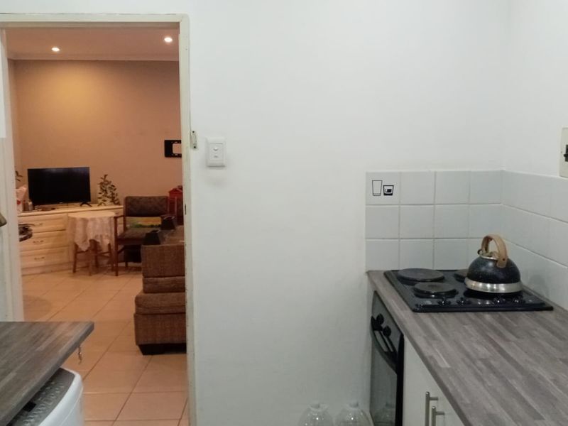 A functional kitchen area featuring a built-in oven, electric hob, laminate countertops, and tiled splashback, with a view into the adjacent living space.