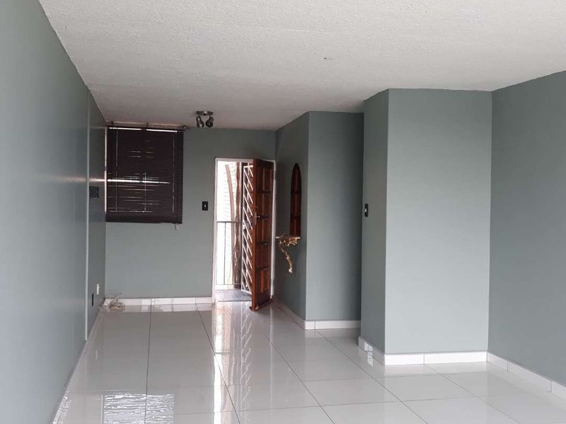 An empty living room featuring white tiled flooring, neutral grey walls, and a security gate leading to an outdoor area.