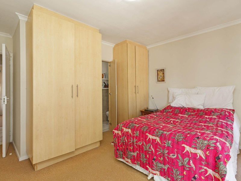 A bedroom featuring light wood built-in cupboards, carpeted flooring, and coved cornicing, with an adjacent en-suite bathroom visible.