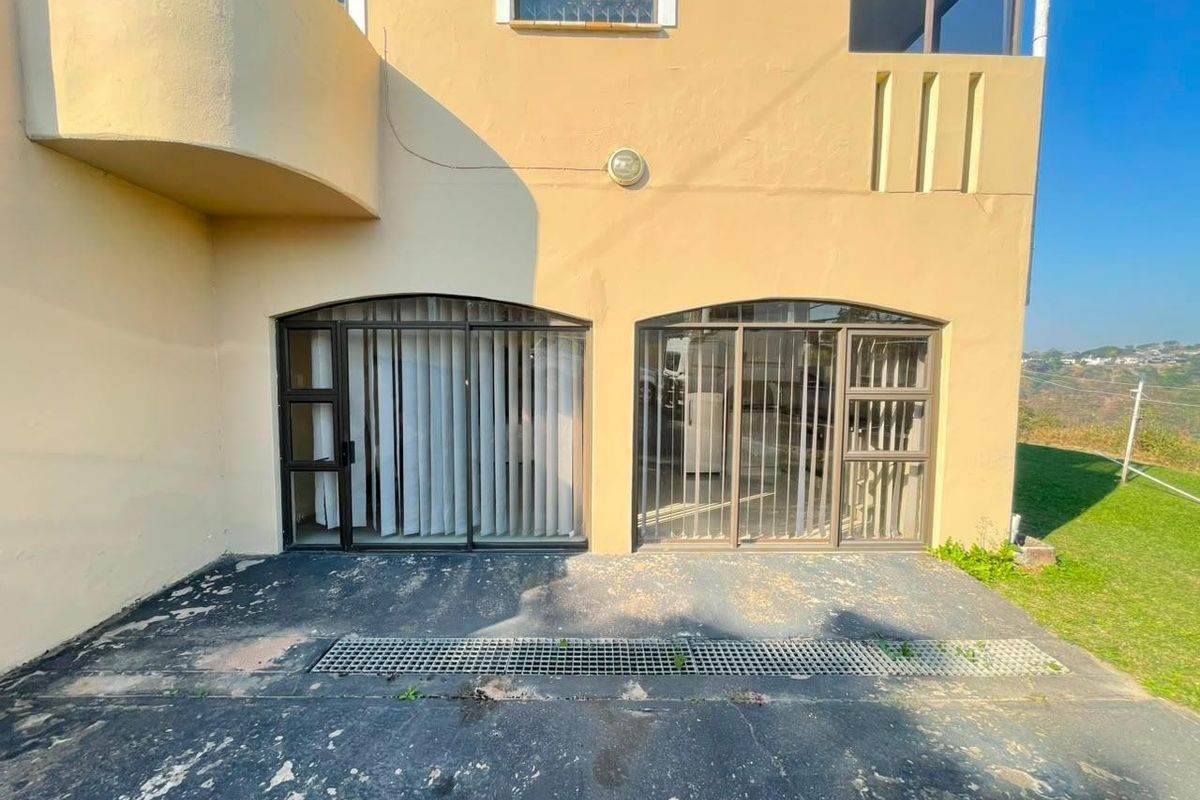 Rear exterior view of the apartment featuring a concrete patio area with sliding glass doors and security bars, showing signs of wear.