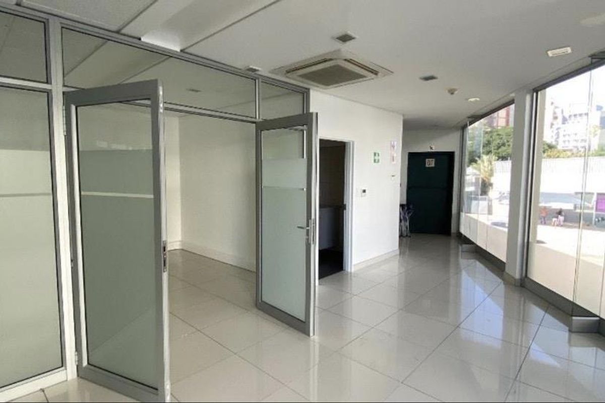 Modern office space featuring aluminum-framed glass partitions, tiled flooring, and large glass windows providing ample natural light.