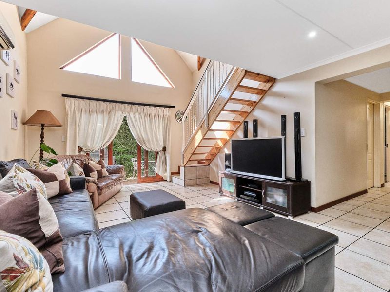 Spacious living room featuring a vaulted ceiling, tiled flooring, and a timber staircase leading to an upper level, with access to the outdoor area.