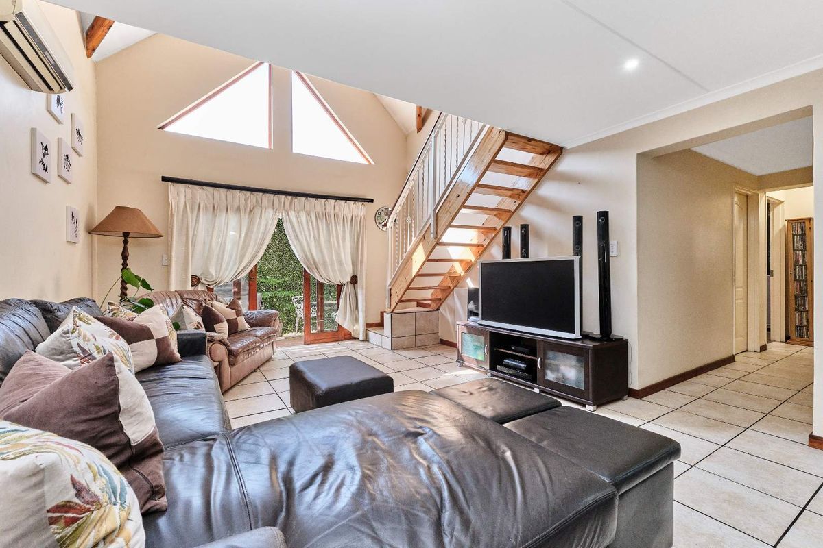 Spacious living room featuring a vaulted ceiling, tiled flooring, and a timber staircase leading to an upper level, with access to the outdoor area.