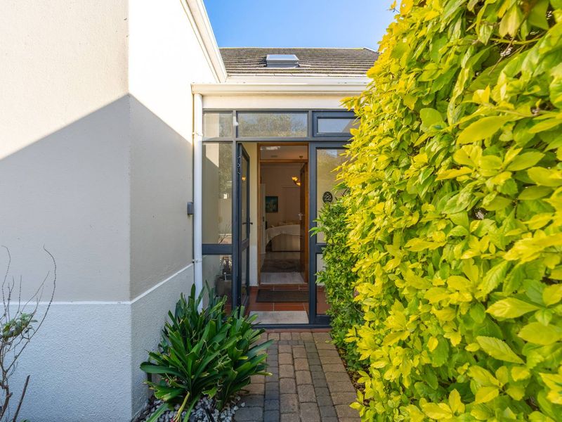 A welcoming front entrance featuring a paved walkway, lush garden hedging, and a glass-panelled door leading into the home.