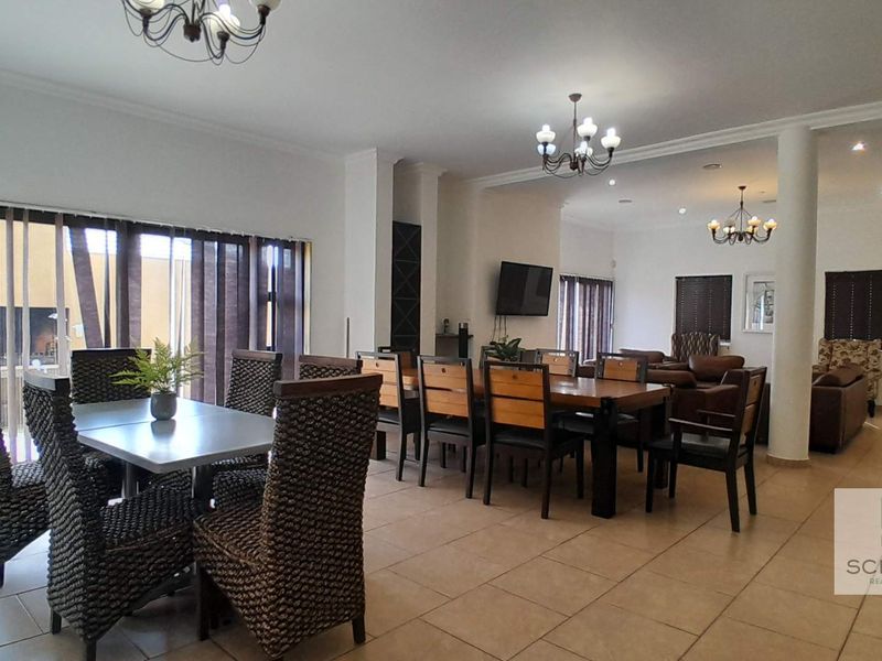 Spacious open-plan living and dining area featuring tiled flooring, multiple chandeliers, and large sliding glass doors providing natural light.