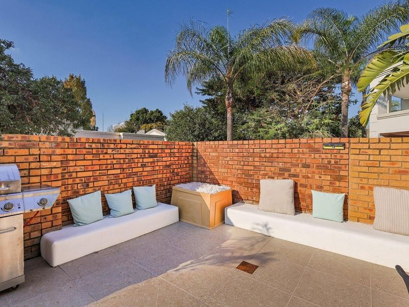 Outdoor patio area featuring a brick boundary wall, built-in concrete bench seating, and a central fire pit on a tiled surface.