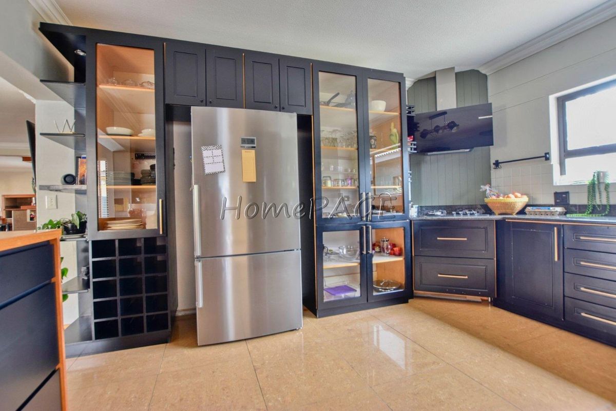 Modern kitchen featuring dark cabinetry, glass-front display units, integrated wine rack, stainless steel refrigerator, and a sleek extractor fan over the cooktop.