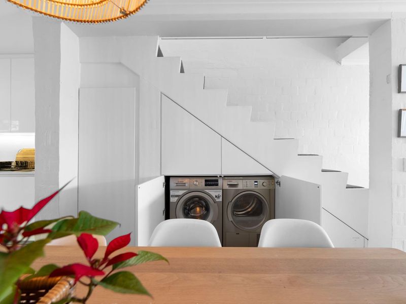 A cleverly integrated laundry area featuring built-in cabinetry and appliances neatly tucked beneath the staircase, maximizing space efficiency in this modern apartment.