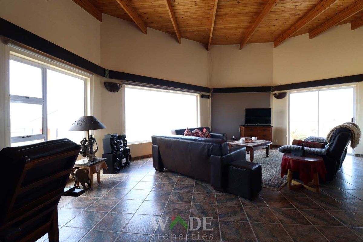 Spacious living room featuring high vaulted timber ceilings, large windows providing ample natural light, and durable tiled flooring.