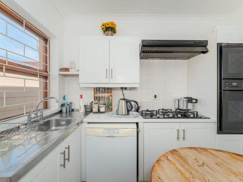 Compact kitchen featuring white cabinetry, stainless steel sink, gas hob with extractor fan, and built-in oven, finished with a tiled splashback.