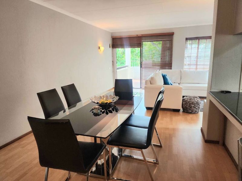 Open-plan living and dining area featuring laminate flooring, neutral walls, and a sliding glass door providing access to an outdoor balcony.