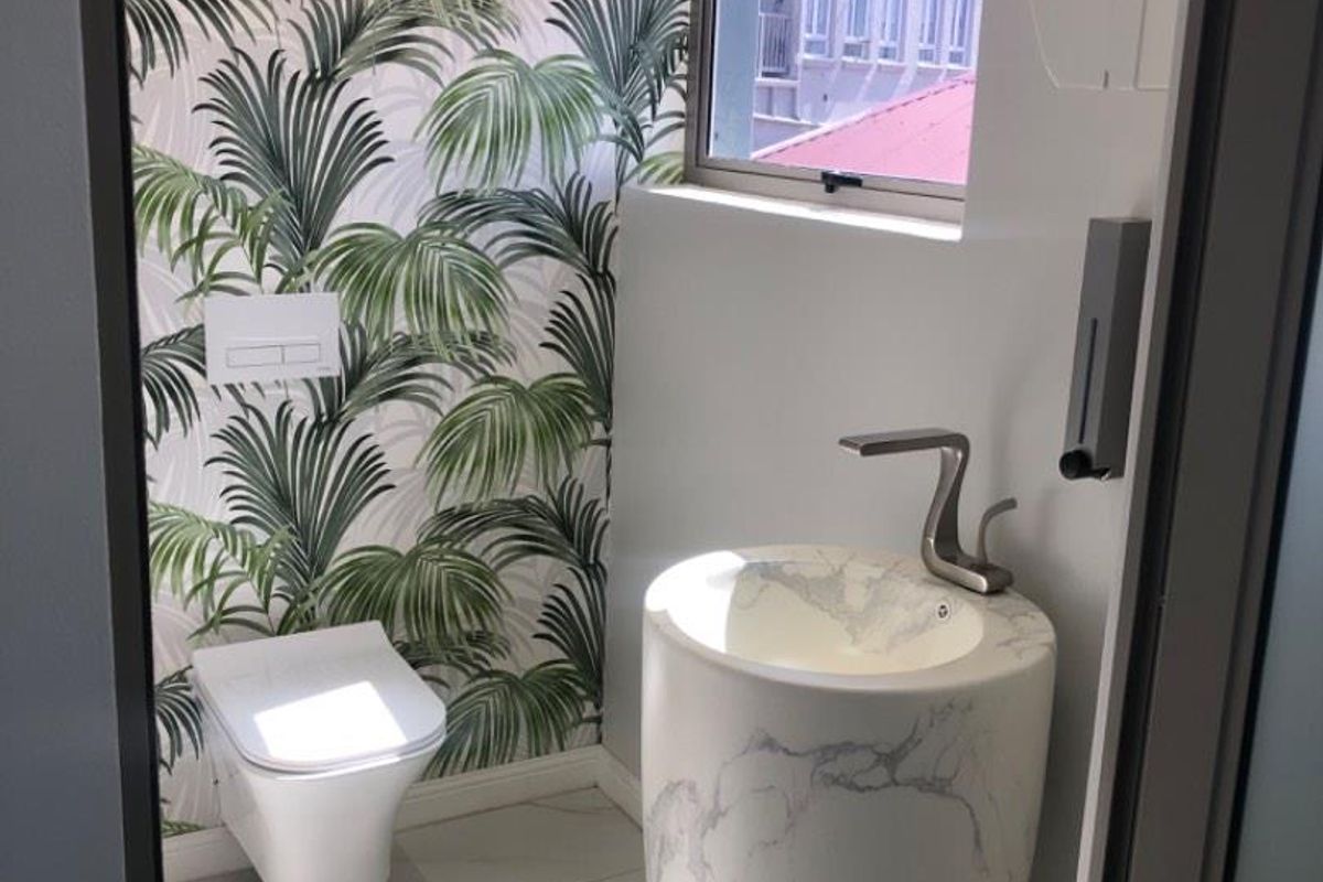 Modern guest bathroom featuring a wall-mounted toilet, a unique marble-effect pedestal basin, and decorative palm-leaf patterned wallpaper.