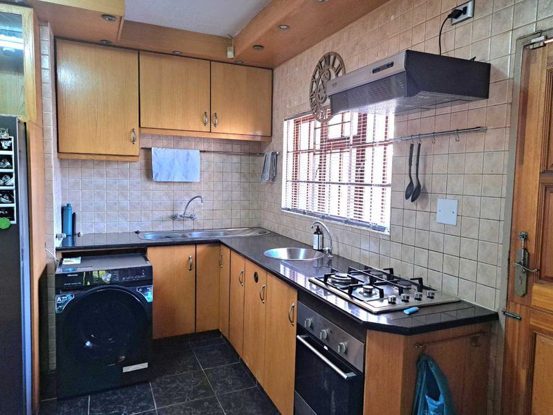 A functional kitchen featuring laminate cabinetry, granite countertops, a gas hob, built-in oven, and tiled finishes throughout.