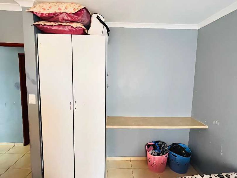 A bedroom featuring tiled flooring, a built-in wardrobe, and a wall-mounted desk, requiring minor cosmetic updates to the wall finishes.