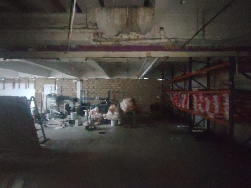 Industrial utility space featuring exposed concrete ceilings, brick walls, and heavy-duty steel racking, currently in need of maintenance and refurbishment.