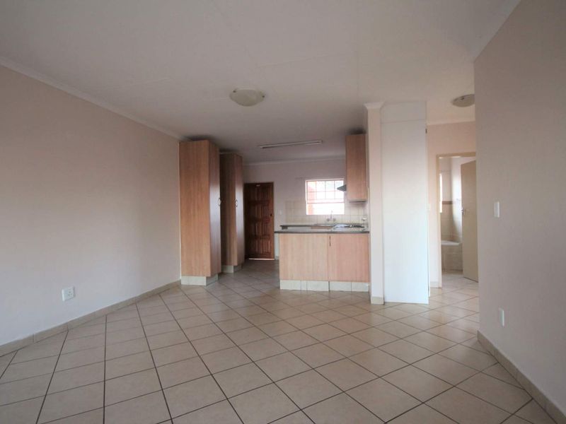 An open-plan living and kitchen area featuring tiled flooring, built-in cabinetry, and a functional kitchen layout in a neutral, well-maintained space.