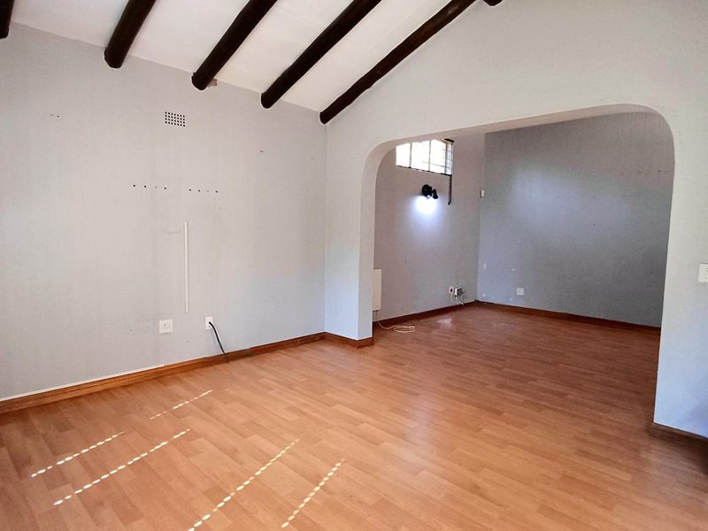 An empty living area featuring exposed timber ceiling beams, laminate flooring, and an arched transition to an adjacent space.