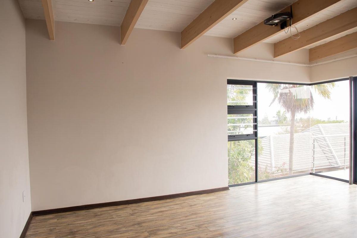 Spacious living area featuring exposed timber ceiling beams, laminate wood flooring, and large corner windows providing ample natural light.