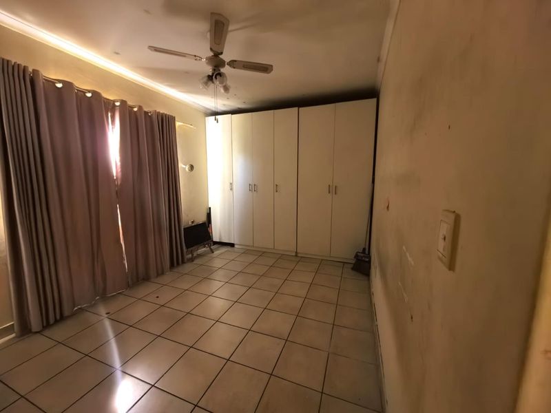 A spacious bedroom featuring built-in cupboards, tiled flooring, and a ceiling fan, requiring cosmetic updates to the wall finishes.