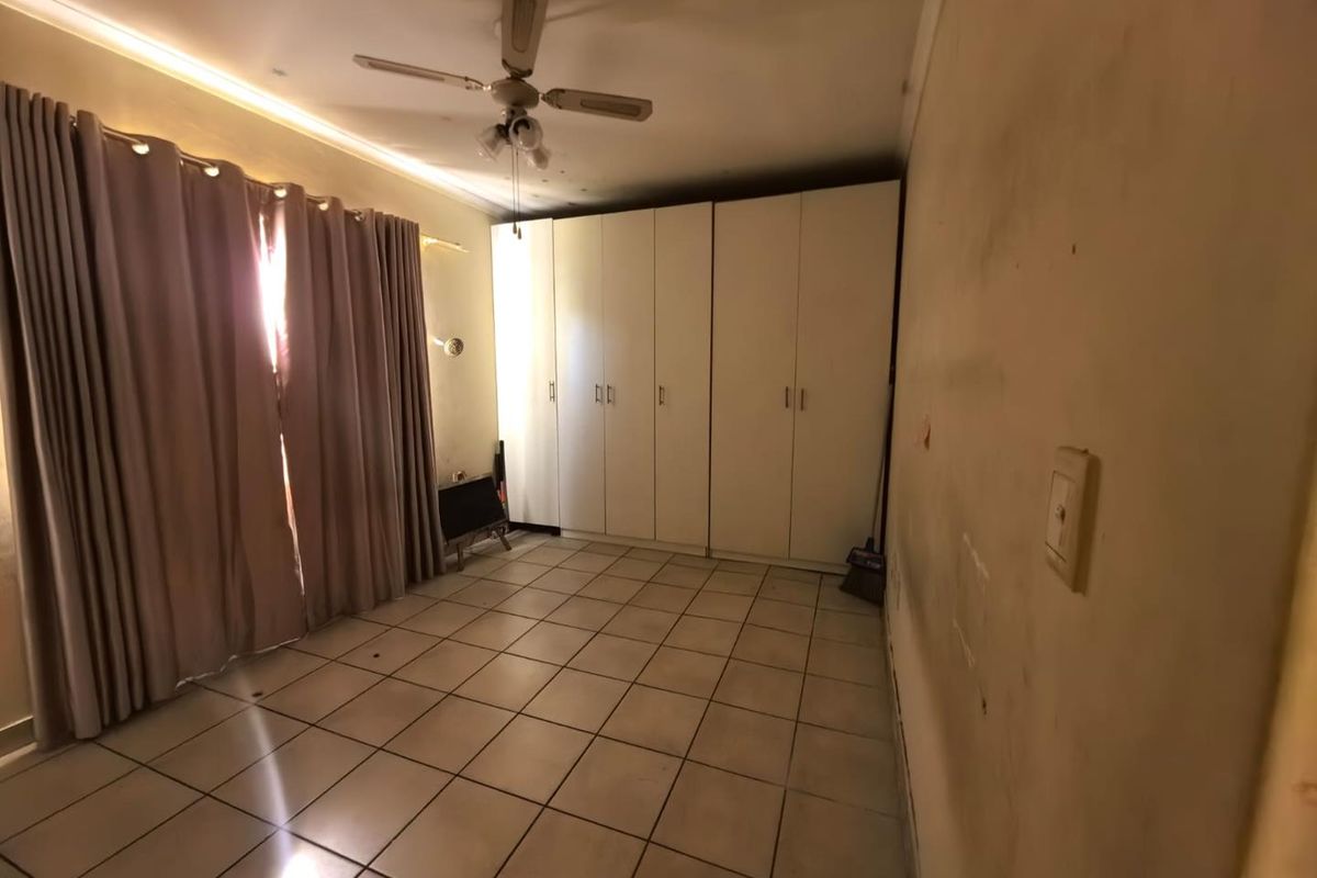 A spacious bedroom featuring built-in cupboards, tiled flooring, and a ceiling fan, requiring cosmetic updates to the wall finishes.