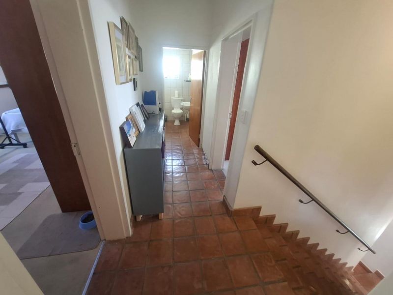 A tiled hallway featuring a staircase with a metal handrail, providing access to adjacent rooms and a bathroom at the end of the passage.