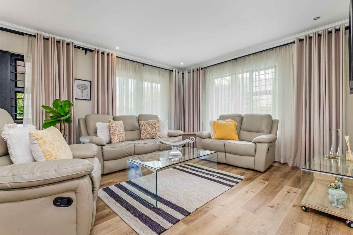 A bright and inviting living room featuring modern wood-look flooring, recessed ceiling lighting, and large windows dressed with elegant floor-to-ceiling curtains.