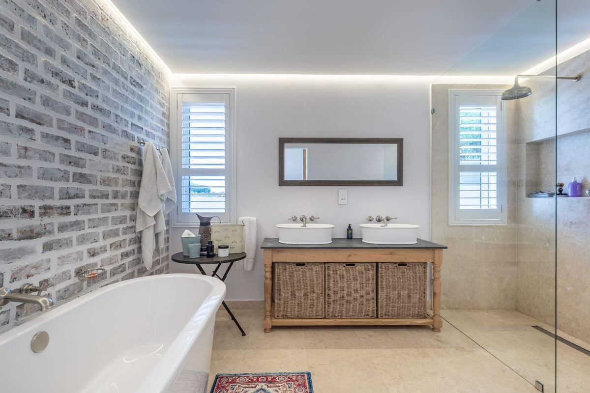 Modern bathroom featuring a freestanding bathtub, double vanity with vessel sinks, walk-in glass shower, and a distinctive exposed brick feature wall.