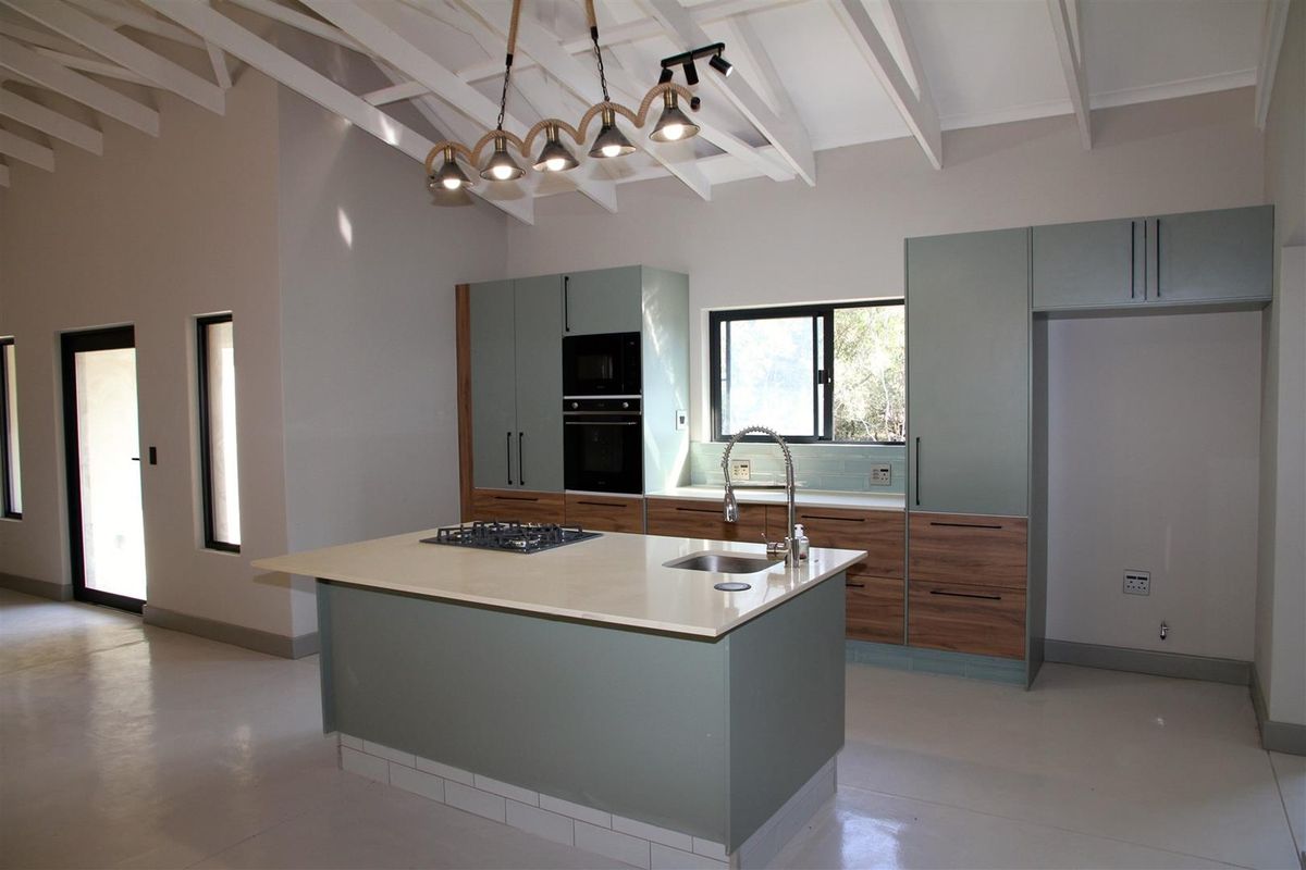 Modern open-plan kitchen featuring a central island with a built-in gas hob, integrated oven, sleek cabinetry, and high vaulted ceilings with exposed beams.
