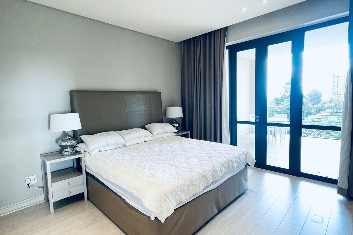 A well-maintained bedroom featuring laminate flooring, recessed lighting, and large glass doors providing direct access to a private balcony.