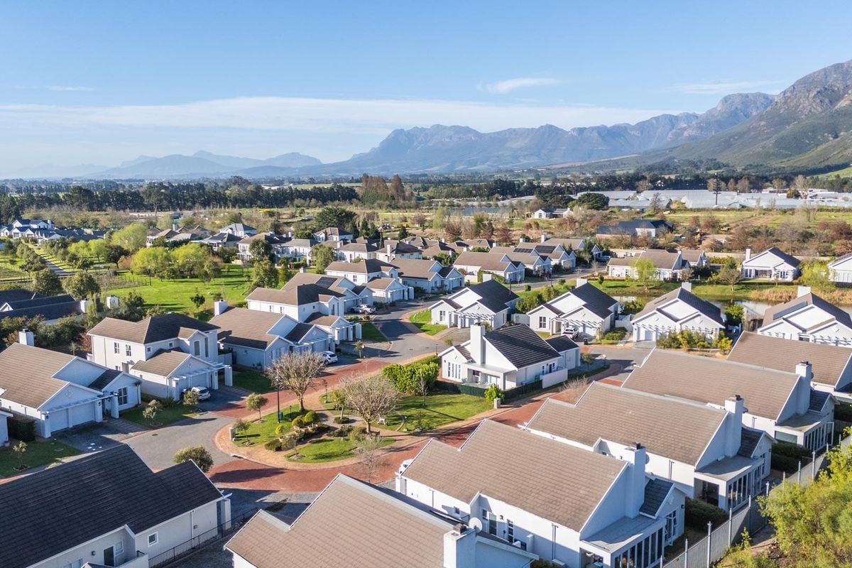 An elevated aerial view of a residential estate featuring multiple detached houses with tiled roofs, surrounded by landscaped grounds and scenic mountain views.