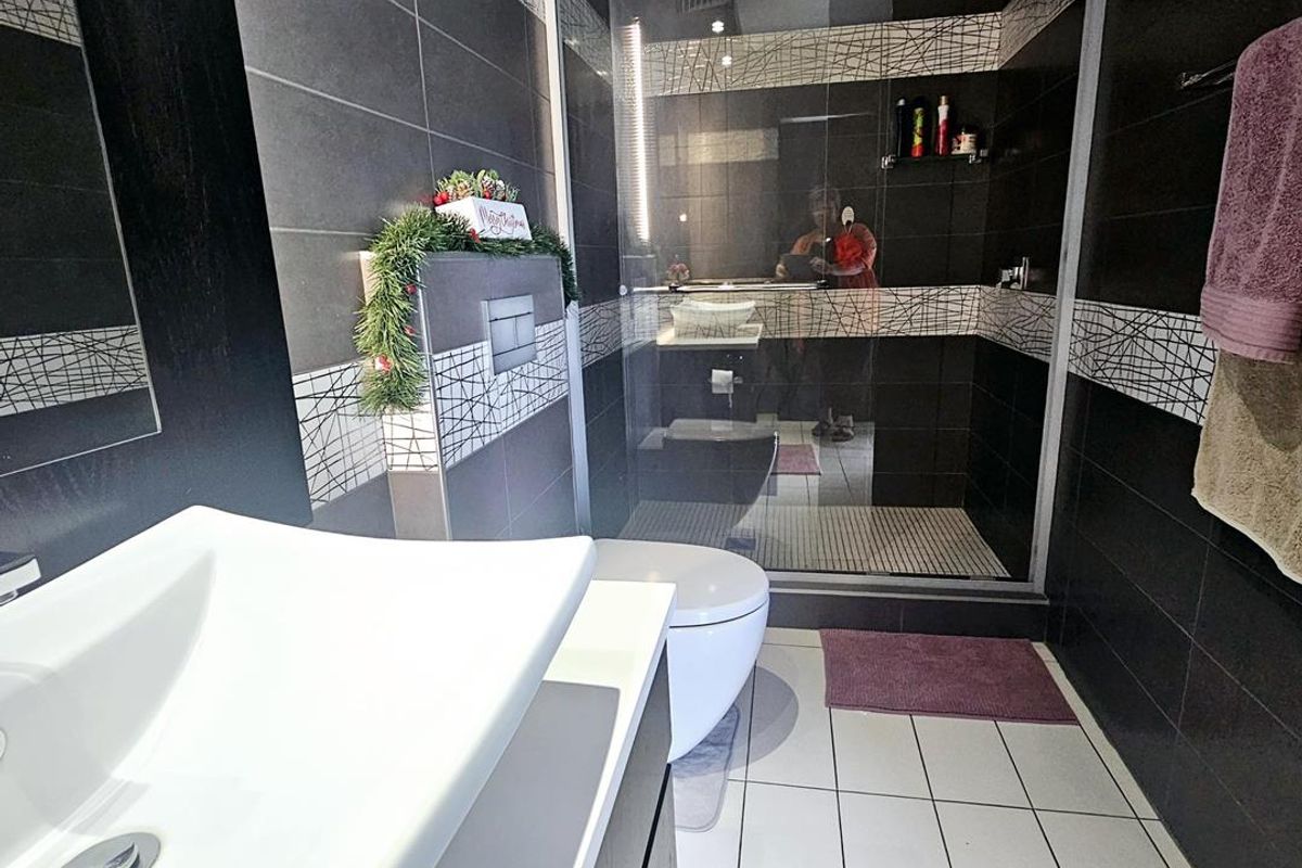 Modern bathroom featuring a glass-enclosed walk-in shower, wall-mounted toilet, and a contemporary vanity basin with dark and light tiled finishes.