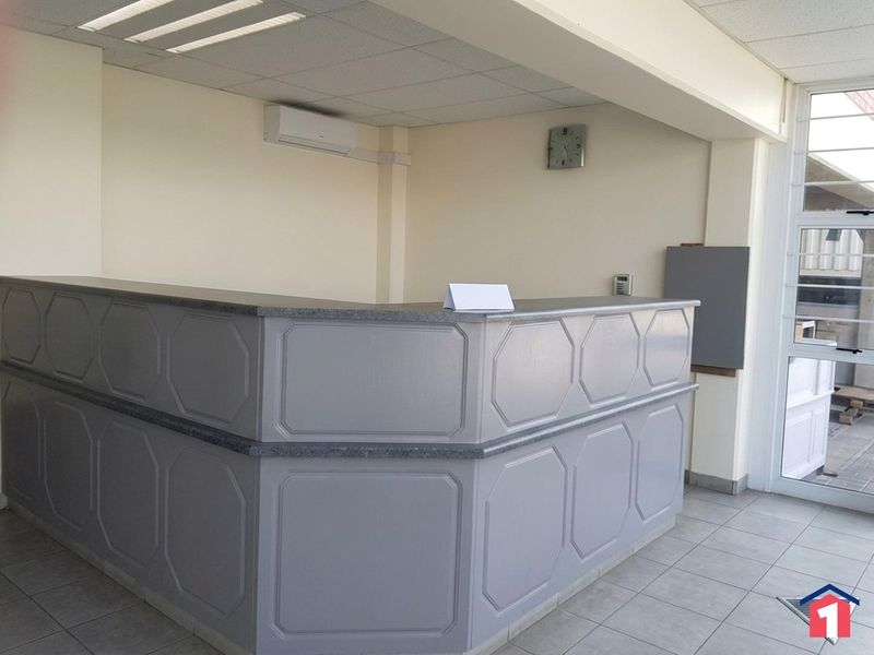 A clean and functional industrial reception area featuring a built-in desk, tiled flooring, suspended ceiling, and integrated air conditioning.
