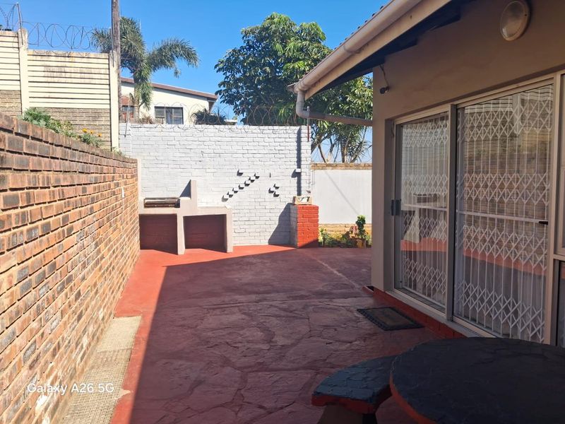 A paved outdoor patio area featuring a built-in brick braai, enclosed by boundary walls with security fencing and direct access to the home.
