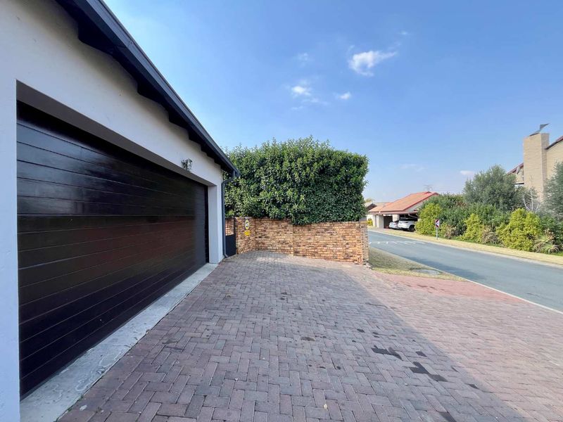 Front exterior view of the townhouse featuring a dark garage door, paved driveway, and a brick boundary wall.