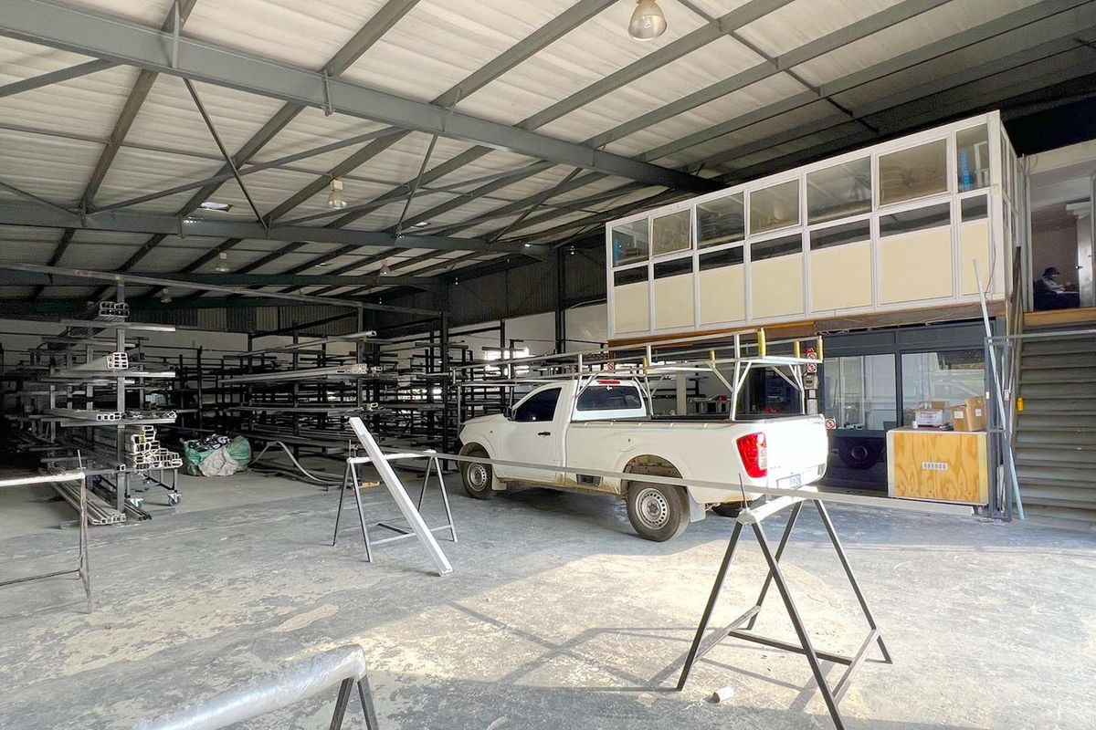 Spacious industrial warehouse featuring exposed steel roof trusses, concrete flooring, and an integrated mezzanine office structure with staircase access.