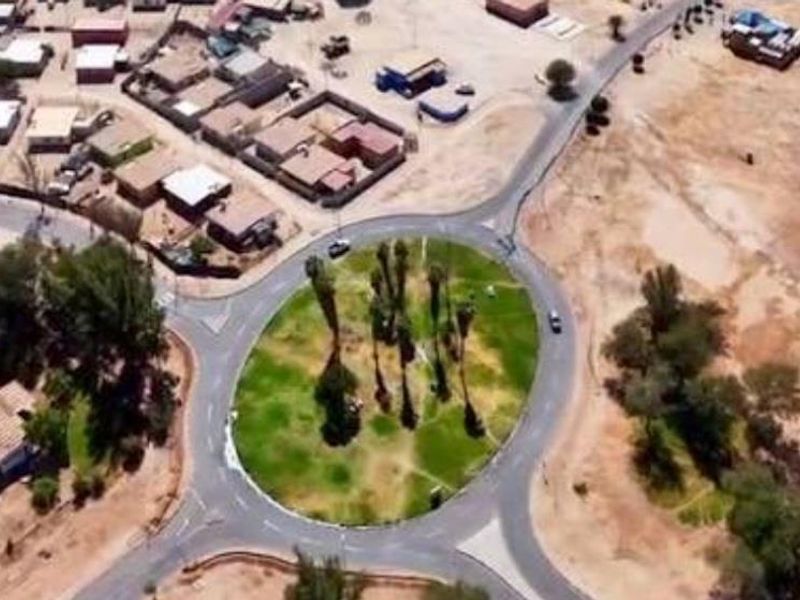 An aerial view of a residential neighborhood featuring a central roundabout with landscaped greenery and surrounding paved road infrastructure.