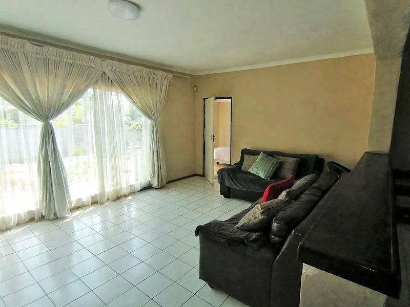 A living room featuring tiled flooring, a built-in counter, and large windows with curtains, offering a functional space with potential for cosmetic updates.