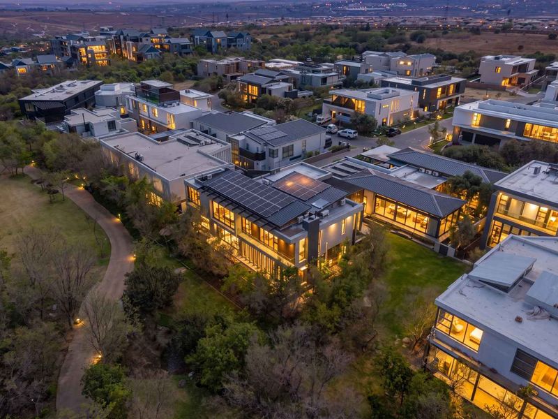 An elevated aerial view of a modern residential estate at dusk, highlighting contemporary architecture, solar panel installations, and landscaped surroundings.