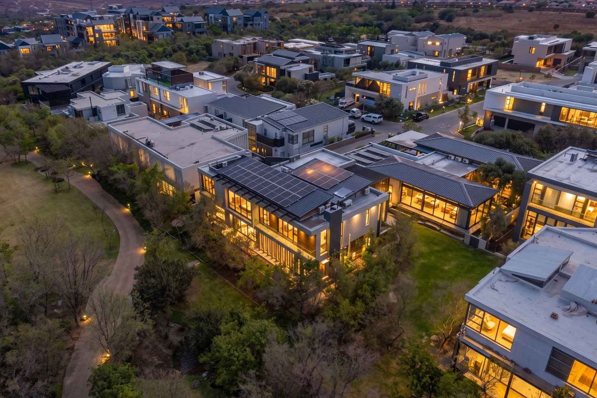 An elevated aerial view of a modern residential estate at dusk, highlighting contemporary architecture, solar panel installations, and landscaped surroundings.