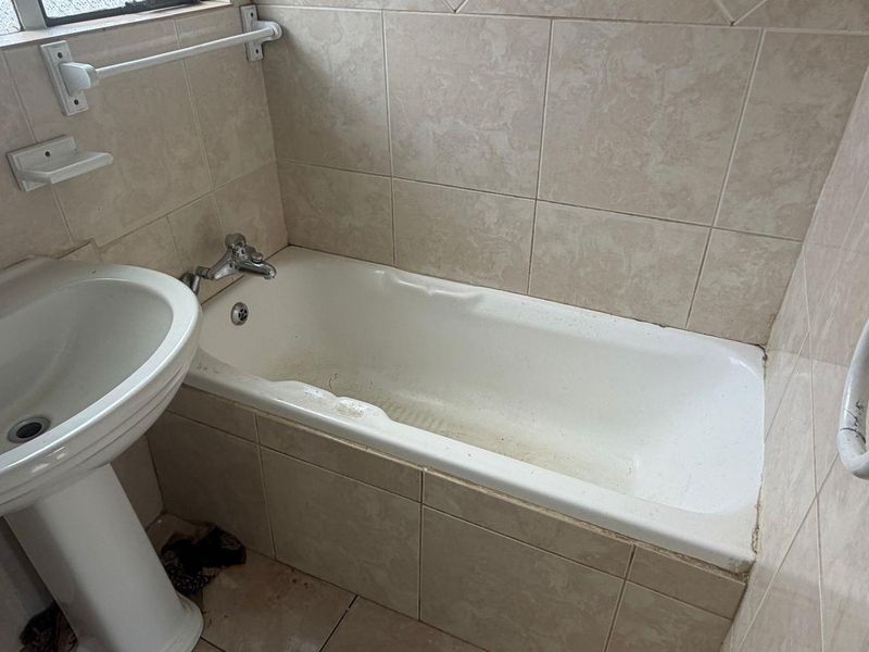 A dated bathroom featuring a pedestal basin and a built-in bathtub with tiled surrounds, requiring cosmetic updates to improve its overall condition.