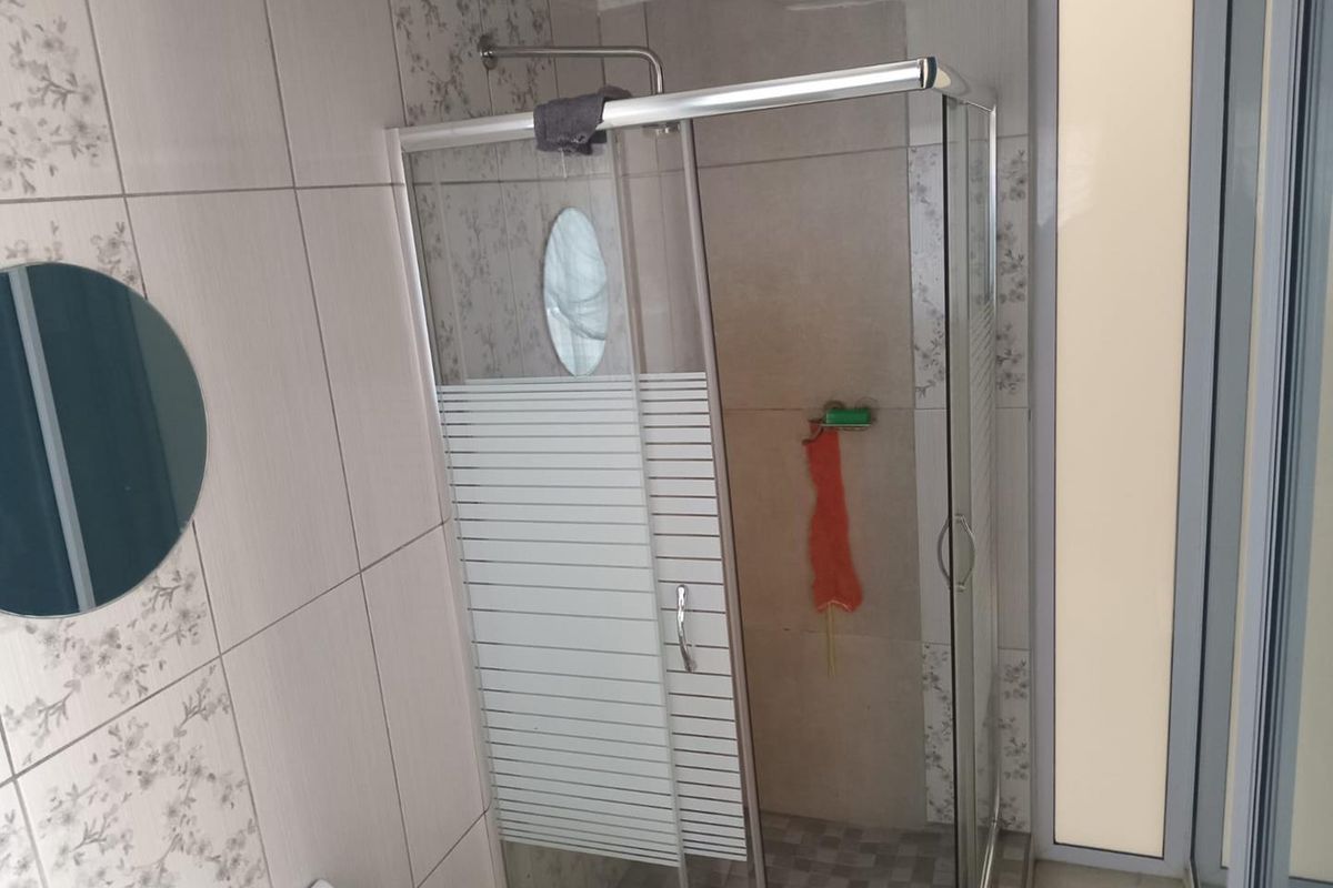 A functional bathroom featuring a corner shower enclosure with glass sliding doors and neutral wall tiling.