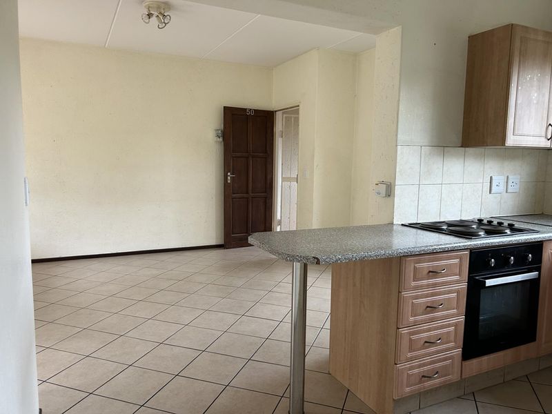 An open-plan living and kitchen area featuring tiled flooring, built-in cabinetry with an integrated oven and hob, and a neutral interior finish.