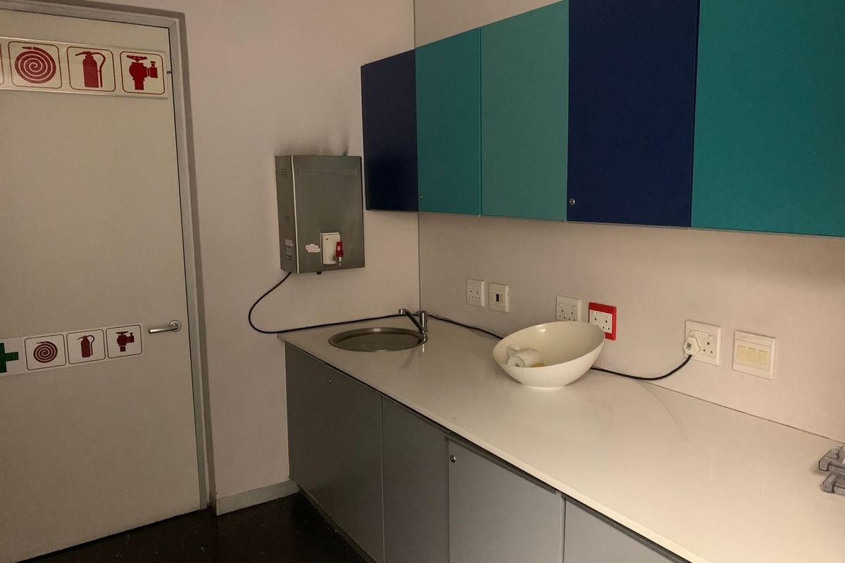 A functional office kitchenette featuring built-in cabinetry, a sink, a wall-mounted water heater, and multiple electrical outlets.