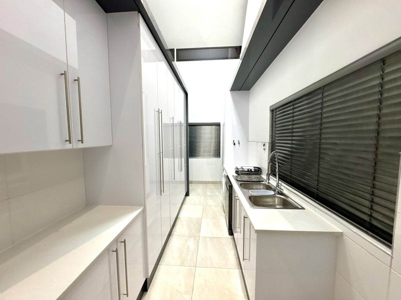 A modern, clean scullery featuring high-gloss white cabinetry, stone countertops, a double stainless steel sink, and neutral floor tiles.