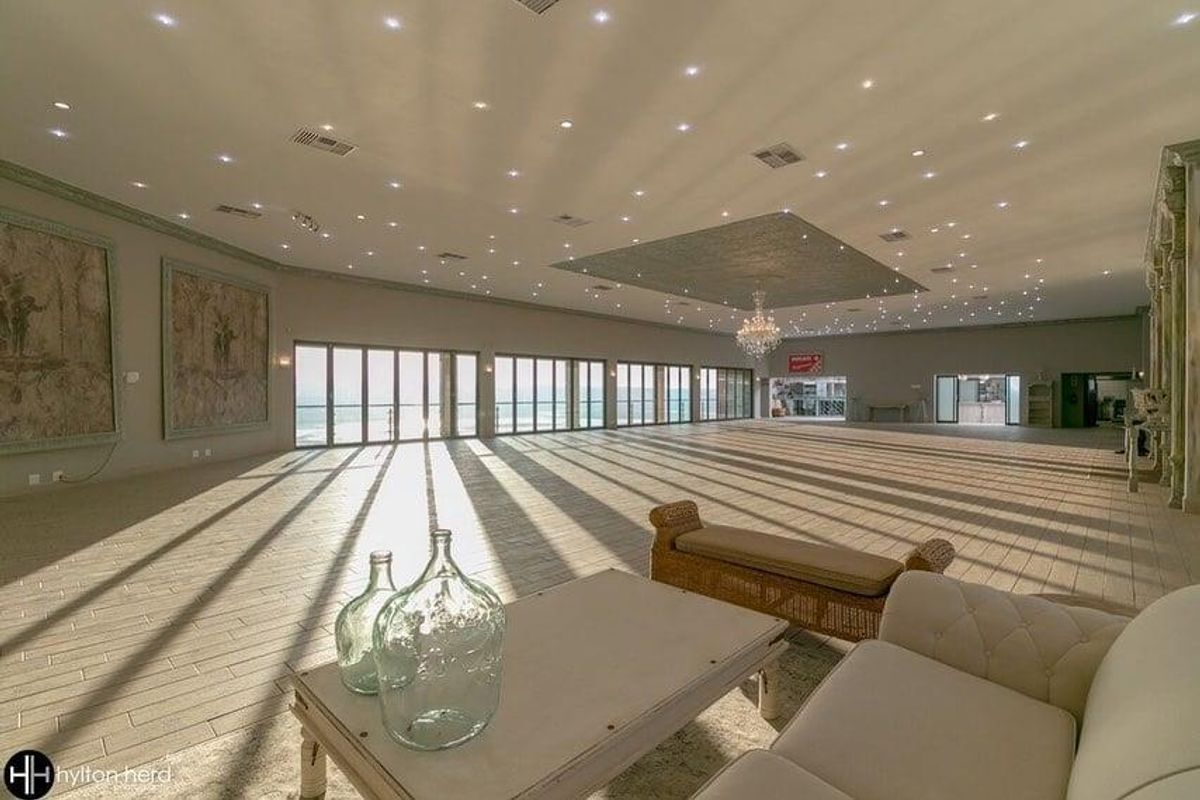 Expansive open-plan living area featuring large format floor tiles, recessed lighting, and extensive folding glass doors offering panoramic views.