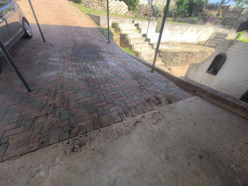An exterior view of a brick paved driveway and carport area featuring concrete stairs leading to a tiered garden section.