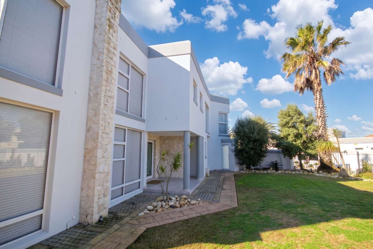 A modern double-storey home exterior featuring stone cladding accents, large aluminium windows, and a well-maintained garden with a paved walkway.