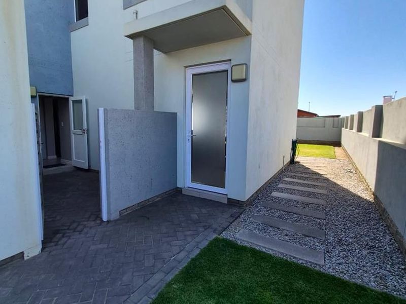 Rear exterior view of the townhouse featuring a paved patio area, a concrete walkway, and a private garden space enclosed by boundary walls.