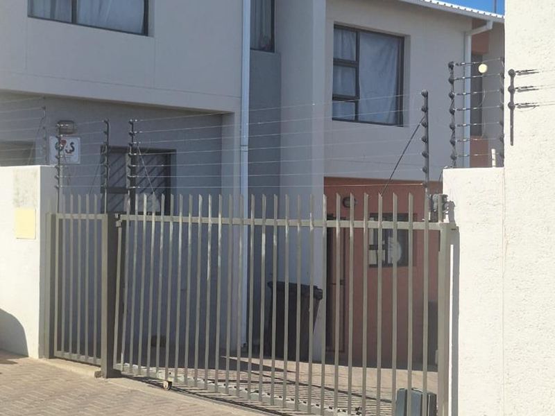 Front exterior view of the apartment complex featuring a secure sliding gate, electric fencing, and paved driveway access.